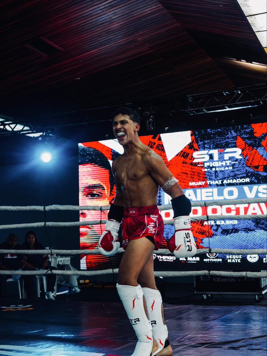 João Octávio no ringue do S1R Fight, de shorts vermelho de muay thai, comemorando.